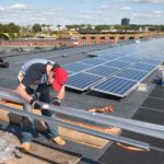 SEEING THE LIGHT: Workers install solar panels last fall on the roof of United Natural Foods. With 192 panels, the solar project is thought to be largest in R.I. to date. / 