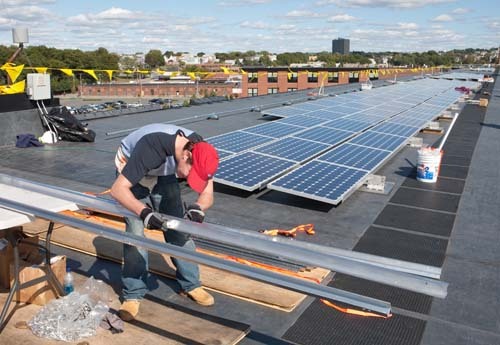 SEEING THE LIGHT: Workers install solar panels last fall on the roof of United Natural Foods. With 192 panels, the solar project is thought to be largest in R.I. to date. / SEEING THE LIGHT: Workers install solar panels last fall on the roof of United Natural Foods. With 192 panels, the solar project is thought to be largest in R.I. to date. /