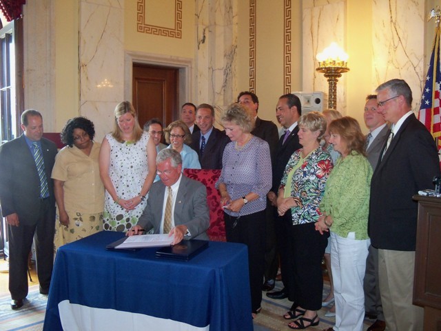 GOV. CARCIERI, surrounded by other officials in the State Room on Tuesday, signs the legislative package to improve the business climate in Rhode Island. / GOV. CARCIERI, surrounded by other officials in the State Room on Tuesday, signs the legislative package to improve the business climate in Rhode Island. /
