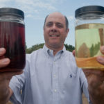 Spreading the gospel on algae as energy source LOOKING AHEAD: Tomorrow BioFuels owner Larry Dressler holds up jars of biocrude, left, and biodiesel. He’s standing at the site of his company’s research building that is under development. /