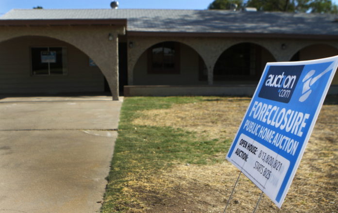AN Auction.com foreclosure sign is displayed outside of a house for sale in Phoenix, Ariz. / BLOOMBERG NEWS FILE PHOTO JOSHUA LOTT