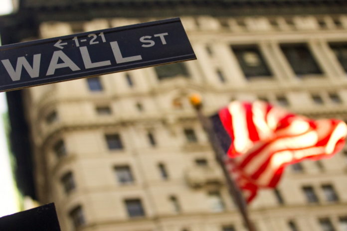A U.S. flag flies behind a Wall Street sign outside of the New York Stock Exchange. / BLOOMBERG NEWS FILE PHOTO JIN LEE