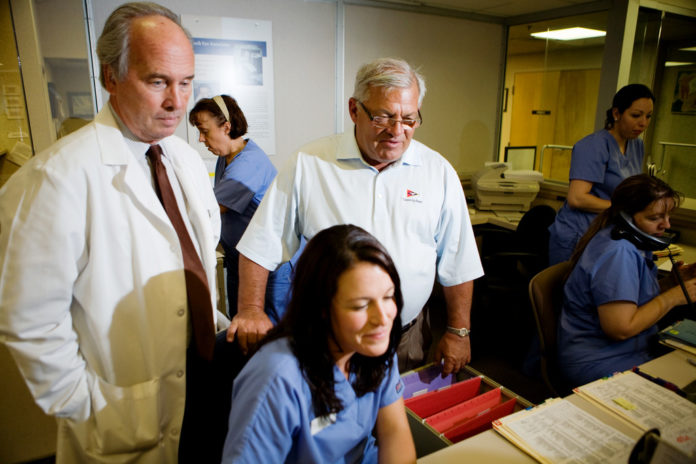 PETER KOCH, center in shirt sleeves, has sold Koch Eye Associates to a private equity firm that is looking to grow the company throughout New England. Also shown in 2010 photo are optician Stephen Grimes, left, and medical secretary Holly Lowe. / PBN FILE PHOTO/RUPERT WHITELEY