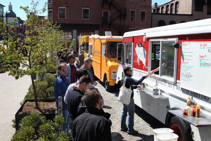 SPECIAL DELIVERY: Customers line up for food at Grant's Block in Providence on April 3. Food Truck Tuesdays have gained popularity in recent months, featuring offerings from Hewtin's Dogs Mobile, Fancheezical and Poco Loco Tacos. / PBN PHOTO/FRANK MULLIN