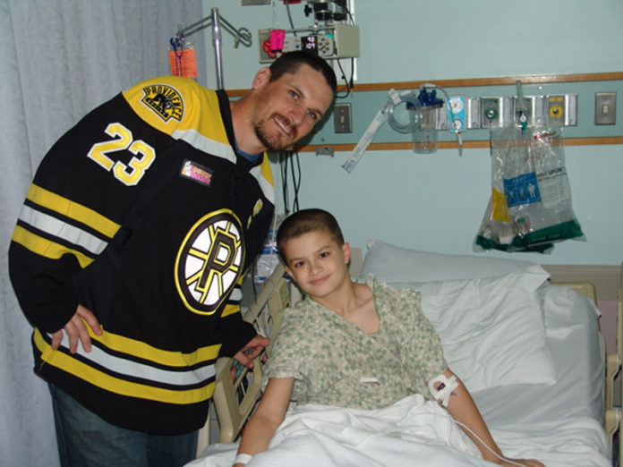 TRENT WHITFIELD, left, center for the Providence Bruins, visits with a patient at Hasbro Children’s Hospital. Whitfield presented a $10,000 donation to the hospital on behalf of his team and Dunkin’ Donuts.