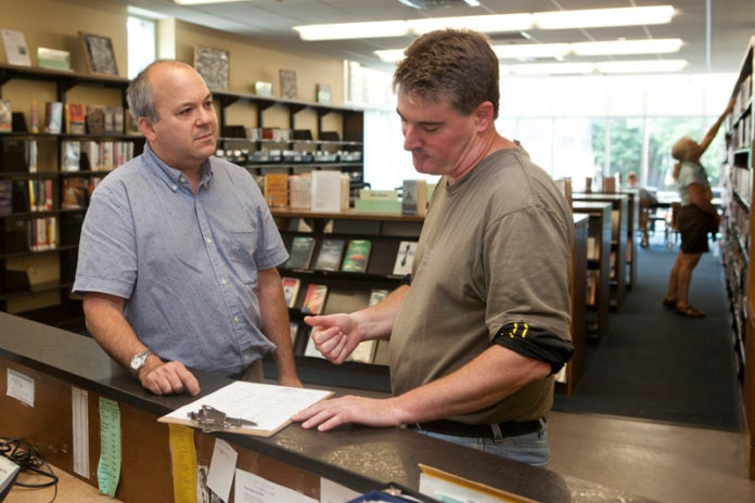 TURNING THE PAGE: Steve Kumins, left, development director of Providence Community Library, speaks with Tim McGinn, circulation supervisor at the Rochambeau Library. / PBN PHOTO/DAVID LEVESQUE
