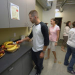 NATURAL SNACKING: Roger Sylvia, left, reaches for a piece of fruit at United Natural Foods&rsquo; break room, part of the company&rsquo;s approach to employee health and wellness. / PBN PHOTO/BRIAN MCDONALD