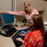 MUTUAL EFFORT: Beacon Mutual Insurance ergonomic consultant Lori Wall, standing, shows nurse consultant Jennifer Nitanya Barlow, how to adjust an ergonomic chair. / PBN PHOTO/NATALJA KENT