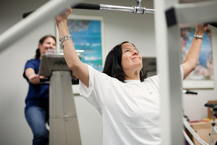 BODY AND HEALTH: Partridge Snow & Hahn employees Ellie Malloy, background, and Robin M. Kuznitz take advantage of the law firm’s on-site gym to meet their fitness goals. / PBN PHOTO/RUPERT WHITELEY