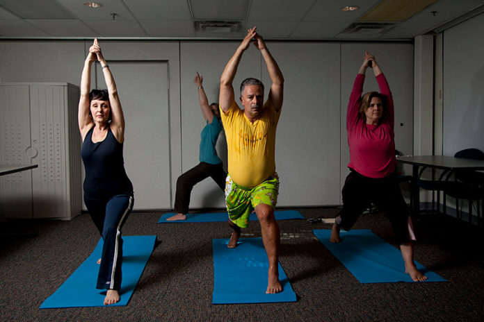 NOT A STRETCH: Care New Englad hosts weekly yoga sessions in its building. Pictured above from left are: executive legal assistant Anna Menna, Santosha Yoga Studio instructor Heather Eilering, Care New England Senior Vice President of Managed Care Domenic F. Delmonico and Associate Vice President and General Counsel Alyssa Boss. / PBN PHOTO/NATALJA KENT