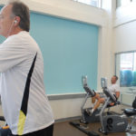 OFFICE WORK: Blue Cross & Blue Shield of Rhode Island has seen an increase in the use of its office fitness center. Above, on the elliptical is William Chartier, Blue Cross communications and instructional designer. In the background is Charles Kineke, company managing director of continuous improvement. / PBN PHOTO/PAUL KANDARIAN