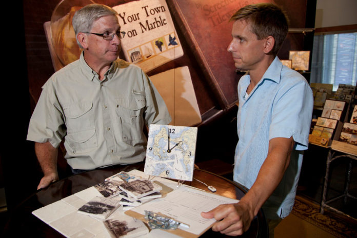 CHARTING A COURSE: Screencraft Tileworks has made vintage maps and nautical charts a focal point of its gift-manufacturing business. Above, company co-owners Trip Wolfskehl, left, and George Abar talk near materials used at a recent trade show. / PBN PHOTO/NATALJA KENT