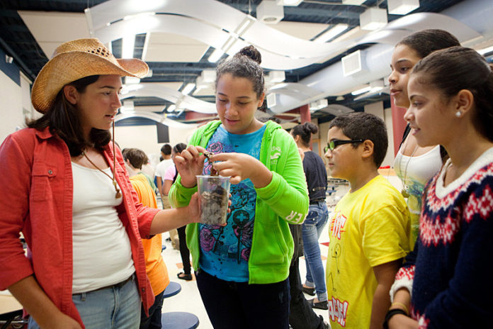 MAKING CONNECTIONS: Middle schoolers at Providence’s Nathan Bishop School, from middle left, Alondra Gomes, Gabriel Rodriguez, Jasmin Fields and Lauren Thornton take part in a PASA AfterZone recruitment fair. In charge of the “Conservation Station” part of the program is Becca Buckler, at left. / PBN PHOTO/RUPERT WHITELEY