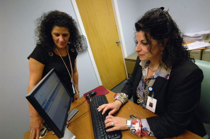 SHINING LIGHT: Cheryl Dumas, health and wellness coordinator and claims co-ordinator, seated, and Robyn Pingitore, claims coordinator, use the new fiber-optic computer system at Fatima Hospital in North Providence. / PBN PHOTO/BRIAN MCDONALD