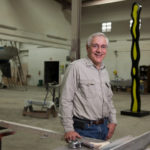 CUSTOM WORK: Paul Amaral, owner of Amaral Custom Fabrications in Bristol, with a sculpture behind him by 1960s pop artist Roy Lichtenstein that the company recently repainted. Amaral worked with Lichenstein for two years before his death in 1997. / PBN PHOTO/DAVID LEVESQUE