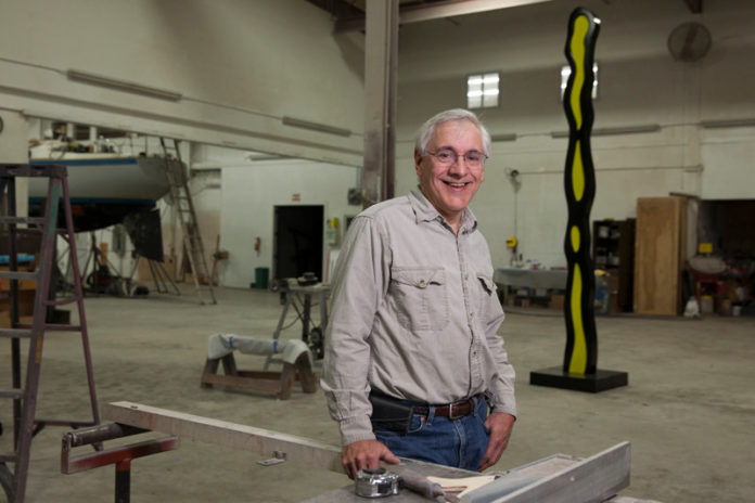 CUSTOM WORK: Paul Amaral, owner of Amaral Custom Fabrications in Bristol, with a sculpture behind him by 1960s pop artist Roy Lichtenstein that the company recently repainted. Amaral worked with Lichenstein for two years before his death in 1997. / PBN PHOTO/DAVID LEVESQUE