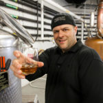 IN GOOD SPIRITS: Mike Reppucci, owner of Sons of Liberty Spirits Co., shows off his whiskey. He makes it in 3,000 square feet of leased space in the Peacedale Mill complex with distilling equipment that includes a 20-foot-tall, 250-gallon Vendome copper still. / PBN PHOTO/DAVID LEVESQUE