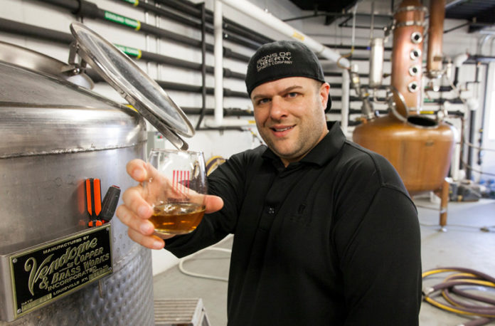IN GOOD SPIRITS: Mike Reppucci, owner of Sons of Liberty Spirits Co., shows off his whiskey. He makes it in 3,000 square feet of leased space in the Peacedale Mill complex with distilling equipment that includes a 20-foot-tall, 250-gallon Vendome copper still. / PBN PHOTO/DAVID LEVESQUE