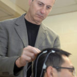 Research emphasis paying off in patents at URI WALTER BESIO, URI engineering professor, who is launching CREMedical Corp., attaches electrodes to the scalp of Ph.D. candidate Xiang Lin. / PBN PHOTO/BRIAN MCDONALD
