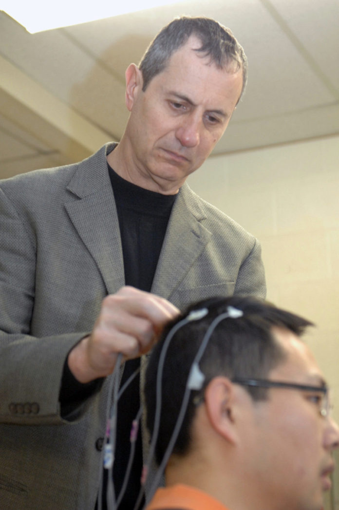 WALTER BESIO, URI engineering professor, who is launching  CREMedical Corp., attaches electrodes to the scalp of Ph.D.  candidate Xiang Lin. / PBN PHOTO/BRIAN MCDONALD