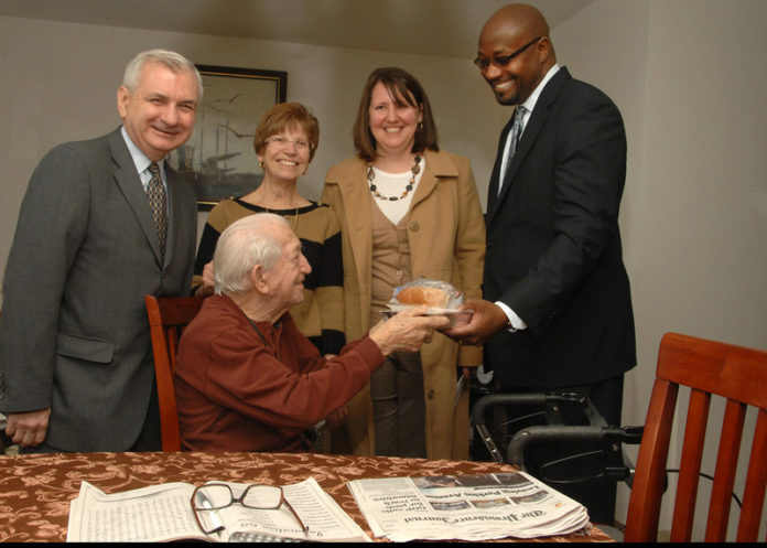 CRANSTON RESIDENT Emilio Rao, seated, receives a meal from CVS Caremark Vice President of Workforce Strategies and Chief Diversity Officer David Casey, right. Also pictured, from left to right, are U.S. Sen. Jack Reed, Rao’s daughter, Lucille Pereschino, and Meals on Wheels of Rhode Island Executive Director Heather Amaral.