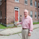 Will tax credits nudge developers? BRINGING IT BACK: Peter Bouchard, Valley Affordable Housing Corp. executive director, in front of Cumberland’s Ashton Mill Village, which the organization hopes to use historic tax credits for. / PBN PHOTO/NATALJA KENT