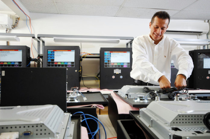 SAFE AND SOUND: Purvis Systems production technician Lee DaSilvachecks on one of the company’s finished products, which are used by public-safety and military organizations across the country to help them respond quickly and efficiently to emergencies. / PBN PHOTO/BRIAN MCDONALD