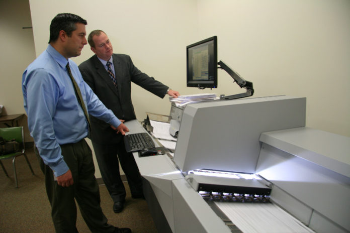BRASS TAX: The R.I. Division of Taxation’s new imaging machine operated by state Tax Administrator David Sullivan, right, and Daniel Clemence, the division’s chief revenue agent and head of e-government efforts. / PBN PHOTO/MICHAEL PERSSON