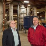 SHOWING METAL: Gannon & Scott CEO Ken Dionne, left, and General Manager Joseph Peixoto in front of the company’s environmental filtration system. This year, the company opened a 93,000-square-foot addition that doubles the Cranston facility’s capacity. / PBN PHOTO/TRACY JENKINS