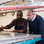 MAKING IT: Anthony Teage, left, an employee at ChemArt, works on a sheet of ornaments while company president David Marquis looks on. / PBN PHOTO/MICHAEL SALERNO