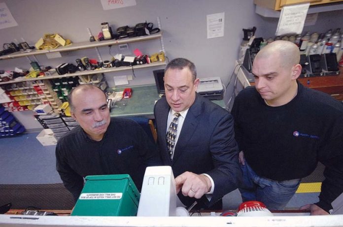 TAKING MEASURES: Apollo Safety President and CEO John Carvalho III, center, leads a training session at the Fall River company. He is pictured above with technician Joseph Bettencourt, left, and John Carvalho IV. / PBN PHOTO/BRIAN MCDONALD