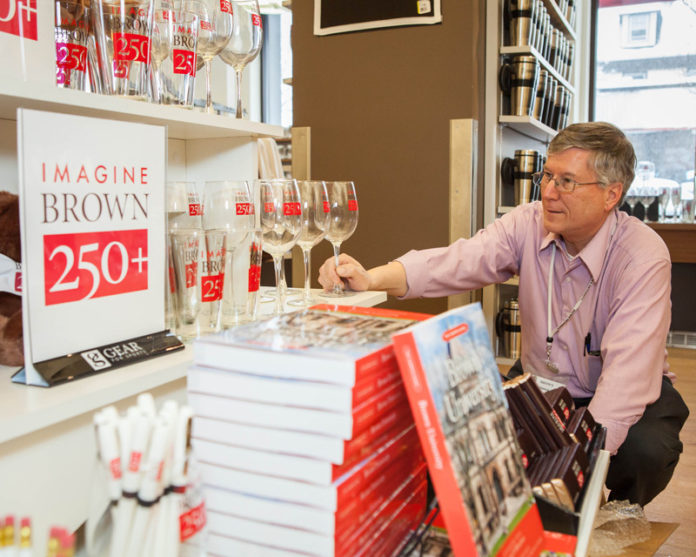 TURNING A PAGE: Ken St. Martin, assistant director of Brown University Bookstore, prepares a display marking the school’s upcoming anniversary. / PBN PHOTO/TRACY JENKINS