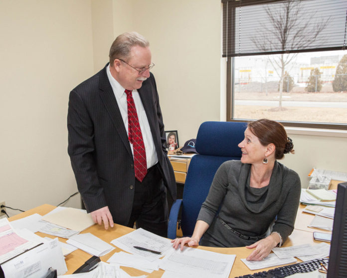 ALL HATS FIT WELL: Kevin Barry, director of finance for the Quonset Development Corporation, has duties far beyond making the numbers work, and he leans on his staff, including Norine Courtemache, an accountant at the quasi-governmental agency. / PBN PHOTO/TRACY JENKINS