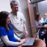 Nurse residency program bridge to employment ON-THE-JOB TRAINING: Amanda St. George, left, shadows nurse Todd Kirschhofer, pictured above, at Thundermist Health Center. Also pictured are Valerie Furr and her mother, Karen Izzo. / PBN PHOTO/MICHAEL SALERNO