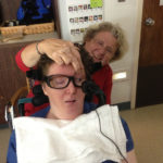 LOOKING AHEAD: Nancy Worthen works with her daughter, Maggie Worthen, seated, using an assistive-technology device developed by SpeakYourMind. / COURTESY DAN BACHER