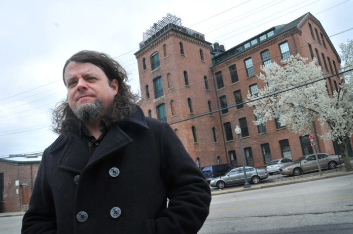 GOING UP? Robert Houllahan, a Providence filmmaker, stands in front of the Monohasset Mill, where he owns a condominium. Houllahan estimates his taxes will go up from approximately $500 per year to as much as $4,000 per year without the stabilization. / PBN PHOTO/FRANK MULLIN