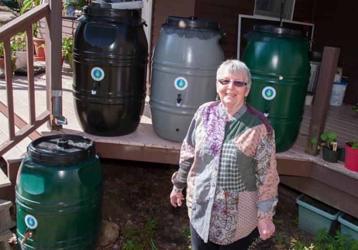 COLLECTIVE THOUGHT: Beverly O’Keefe, owner of Rhode Island Water Lady, a small business that sells rain barrels, stands next to one she has installed at home. / PBN PHOTO/MICHAEL SALERNO