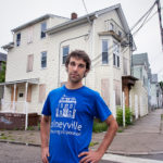 CAN&rsquo;T GO HOME: Chris Ackley, stewardship manager at Olneyville Housing Corp., in front of 238 Amherst St. in Olneyville. The three-family home has yet to be foreclosed on because banks don&rsquo;t want to own it. / PBN PHOTO/MICHAEL SALERNO