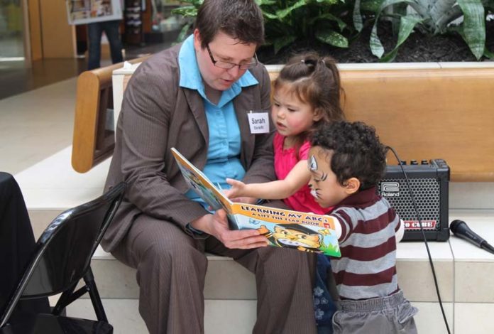 SARAH CLAUSIUS-PARKS, branch manager at Bank Rhode Island’s Downtown Providence office, reads with two children during the literacy event at Warwick Mall.