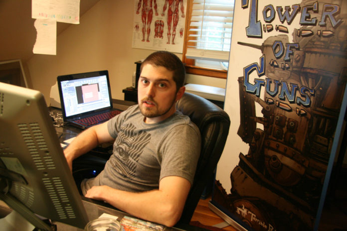 EXTRA LIFE: Former 38 Studios artist Joe Mirabello sits at his work station in Sharon, Mass., where he designed his own game, “Tower of Guns.” Mirabello spent almost two years after the close of 38 Studios programming and designing the game. / PBN PHOTO/MICHAEL PERRSON
