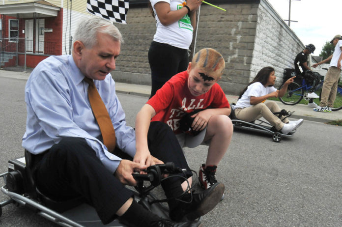 OUTSIDE THE BOX: Serving mainly city kids from less-privileged neighborhoods, the Center for Dynamic Learning looks to help children who are not thriving in traditional classrooms. Above, U.S. Sen. Jack Reed takes instruction from Samuel Cunha, red shirt, and Krystalee Diaz Nieves prepares to start cart racing at the Center for Dynamic Learning’s End-of-Session Celebration at Culcutt Middle School in Central Falls. / PBN PHOTO/FRANK MULLIN
