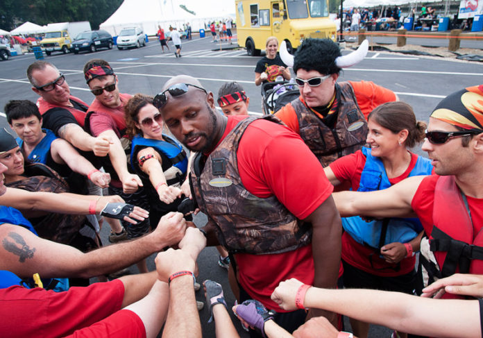 PEAK PERFORMANCE: Kerry Taylor, center, owner of 212 Health & Performance, leads the Fire On The Water team in an inspirational huddle before the 2014 Dragon Boat Races in Pawtucket. / PBN PHOTO/MICHAEL SALERNO
