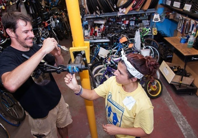 MAKING CONNECTIONS: Gina Cincotta, a freshman at Roger Williams University majoring in marine biology, works at Recycle-a-Bike for Community Connections Day. At left is Recycle-A-Bike Program Director Patrick McEvoy. / PBN PHOTO/MICHAEL SALERNO