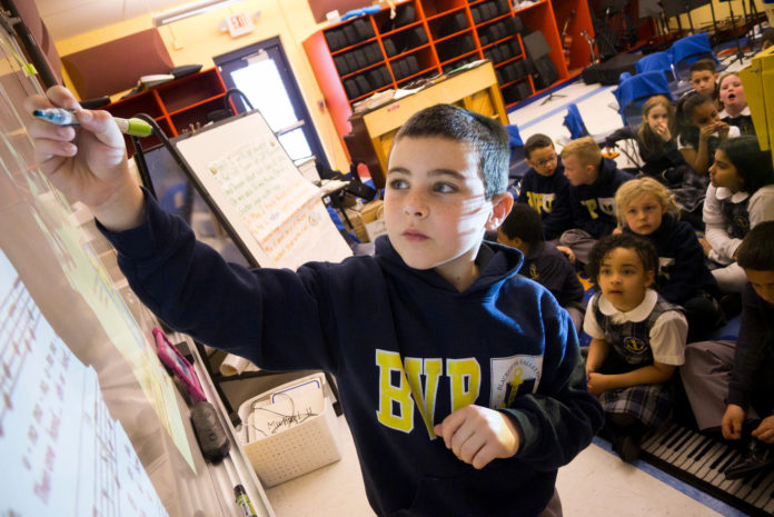 PROBLEM SOLVING: Founded in 2009, Blackstone Valley Prep Mayoral Academy has prospered despite opposition to expansion of charter schools in Rhode Island from local teacher unions. Above, Blackstone Valley Prep Mayoral Academy second grader Daniel Marino works out a problem on an interactive whiteboard with his classmates. / COURTESY JONATHAN BELLER