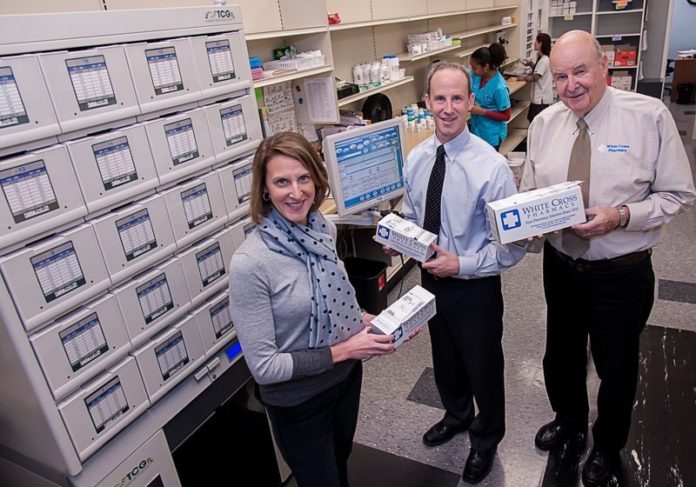 North Providence’s White Cross Pharmacy has grown into a third-generation, family-owned business serving clients in three states by constantly working to meet the changing needs of customers. From left, Beth Brown, business director; Robert J. Iacobucci, pharmacy director and  Robert L. Iacobucci, company president and CEO, show off one of the latest examples, the Med Box. The containers hold all of a patient’s medications, which are organized for them by day and hour. The company’s clients include assisted-living facilities and group residential homes. / PBN PHOTO/MICHAEL SALERNO