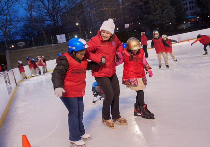 COLD ICE, WARM HEART: Carolyn Drumm, executive director of nonprofit Skate For Joy, helps Andreina Dominguez, left, and Namrita Riat out onto the ice at the Alex and Ani City Center skating rink at Kennedy Plaza in Providence. / PBN PHOTO/MICHAEL SALERNO