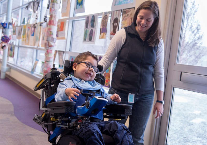 VIRTUAL REALITY: Ryan Hebert, 5, works with physical therapist Megan Wilkins at Meeting Street in Providence. Ryan uses head movements to operate his chair. / PBN PHOTO/MICHAEL SALERNO