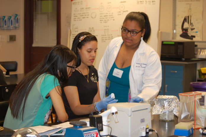 JUANITA SANCHEZ High School junior Perla Castillo, right, provides guidance to classmates Sorielisa De La Cruz and Yasiry Munoz during a recent biotechnology workshop at the University of Rhode Island Providence Biotechnology Center.