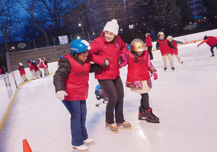 COLD ICE, WARM HEART: Carolyn Drumm, executive director of nonprofit Skate For Joy, helps Andreina Dominguez, left, and Namrita Riat out onto the ice at the Alex and Ani City Center skating rink at Kennedy Plaza in Providence. / PBN FILE PHOTO/MICHAEL SALERNO