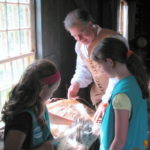 PETER GIAMMARCO demonstrates recently how flax is prepared for spinning as Abigail Goncalves, left, and Elizabeth Lambert help at the Smith-Appleby House in Smithfield. The historic building is one of 29 in the Rhody Ramble program, which has four new members. The program provides exposure to hands-on activities for families. / COURTESY DON GONCALVES